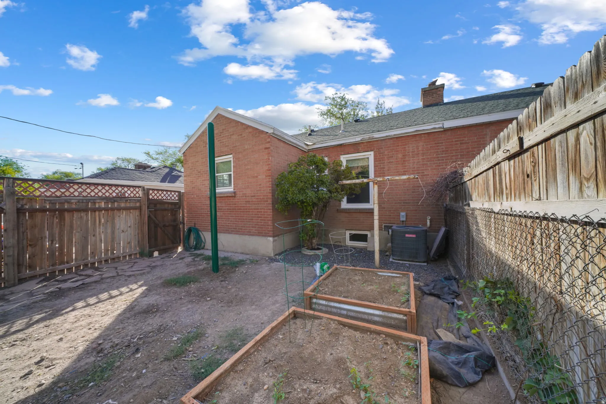 Brick exterior with multiple windows, wooden privacy fencing, chain link fencing, and raised garden beds