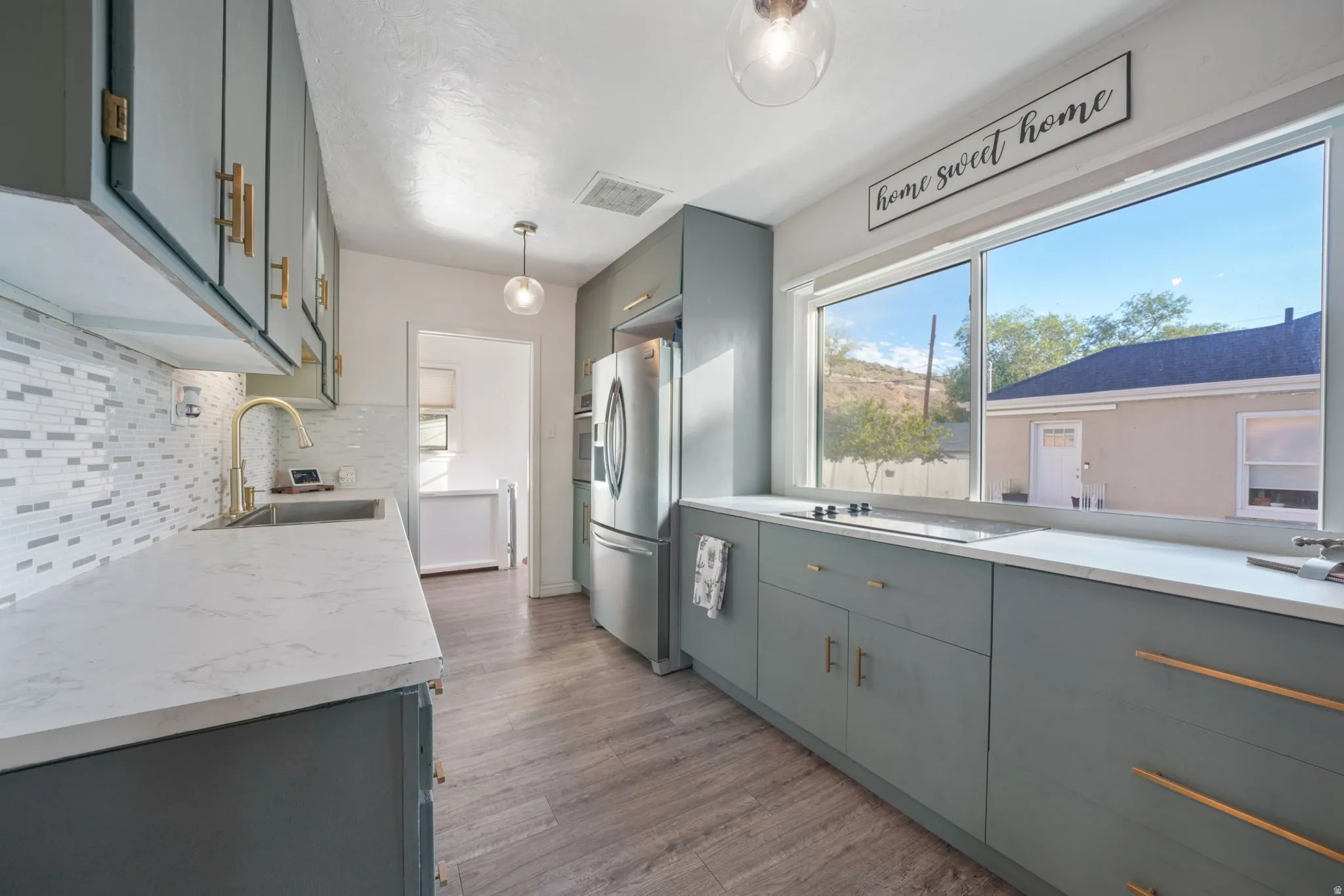 Kitchen featuring wood-finish flooring, light-toned cabinetry with gold-tone hardware, and a white countertop