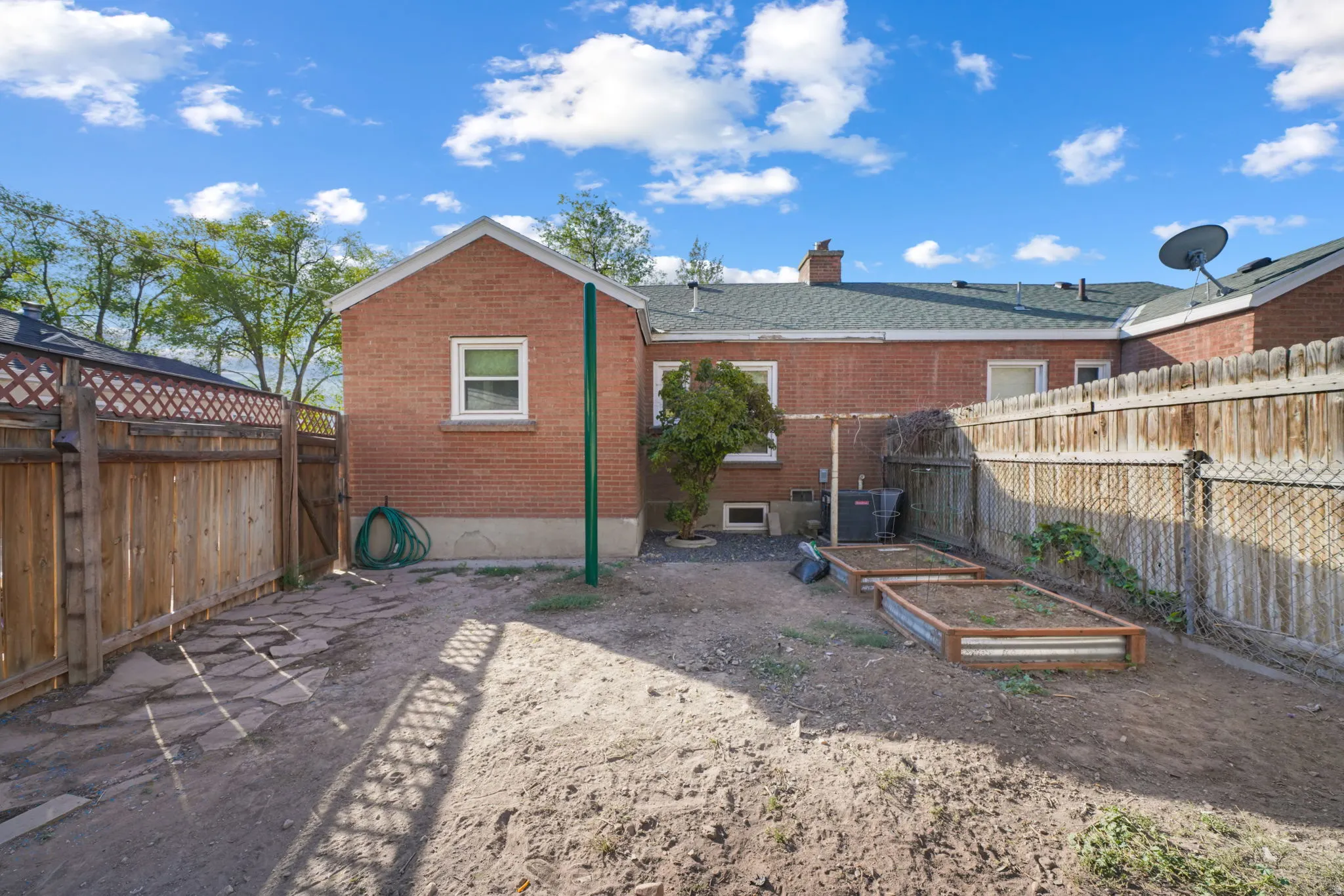 Enclosed backyard featuring a wood fence, flagstone path, and raised garden beds