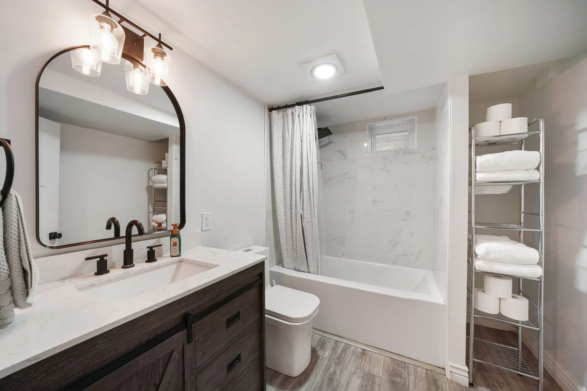 Vanity with quartz countertop and undermount sink, dark wood-finish cabinetry, matte black fixtures, and wood-finish flooring