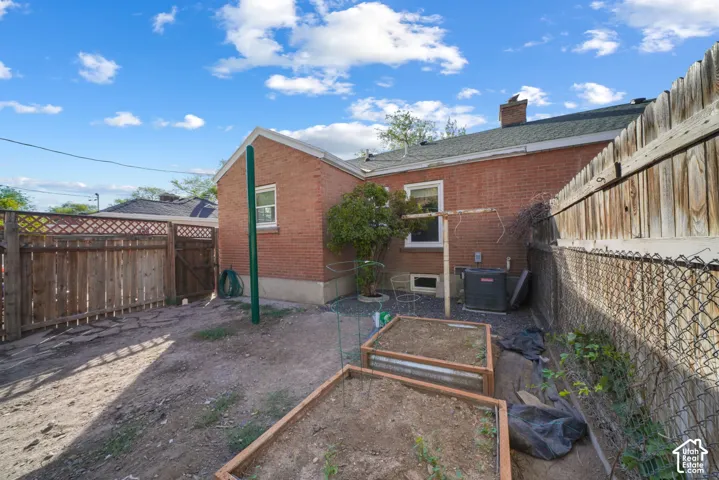 Brick exterior with multiple windows, wooden privacy fencing, chain link fencing, and raised garden beds