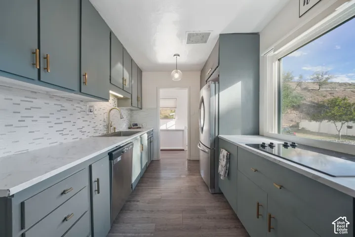 Galley kitchen featuring matte blue cabinetry with gold-toned hardware, light-toned countertops, tile backsplash, and stainless steel appliances