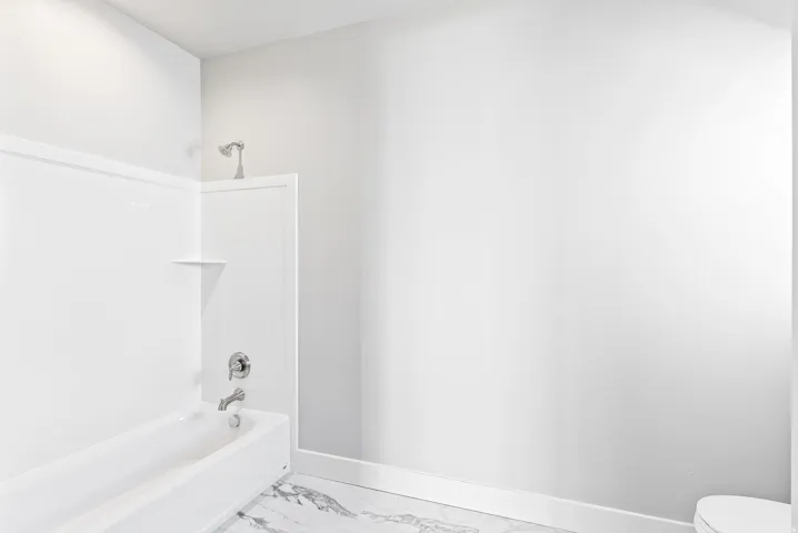 White tub and shower combination with chrome fixtures and integrated shelving