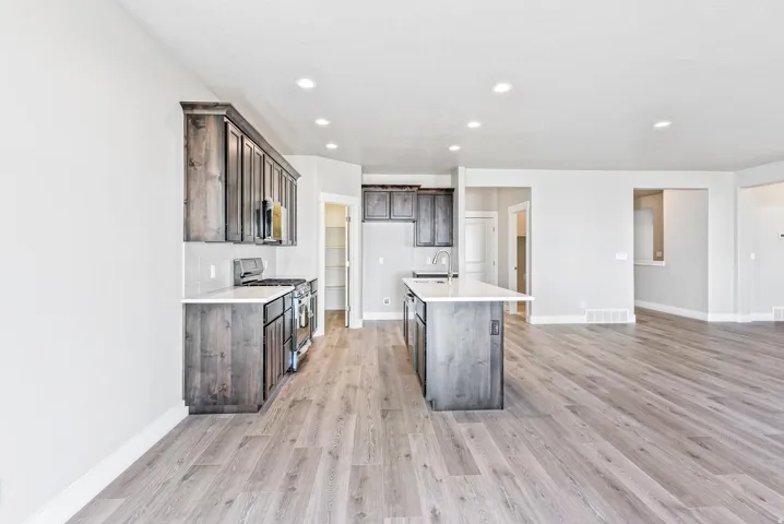 Kitchen featuring dark wood-finish cabinetry, stainless steel appliances, a center island with a sink, and light countertops