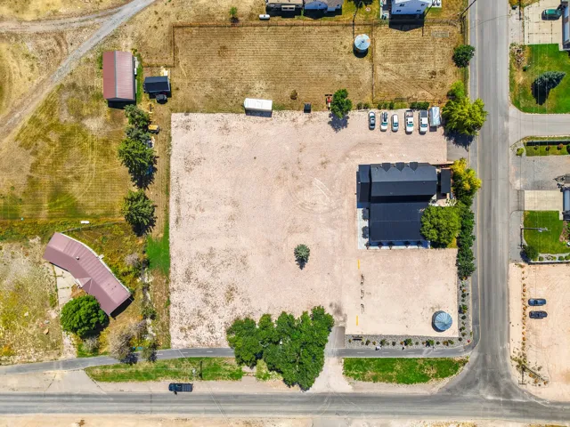 Expansive gravel lot featuring a large commercial-style building with a black roof, additional outbuilding, and mature trees