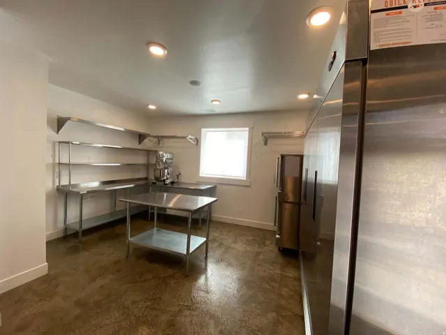 Polished concrete flooring, stainless steel shelving, recessed ceiling lighting, a window with a white frame, and a stainless steel commercial refrigerator