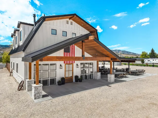 Modern barn-style architecture featuring dormer windows, a black metal roof, and a covered patio with exposed wood beams