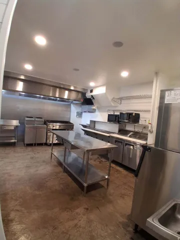 Stainless steel commercial kitchen with a large exhaust hood, recessed lighting, and a concrete floor