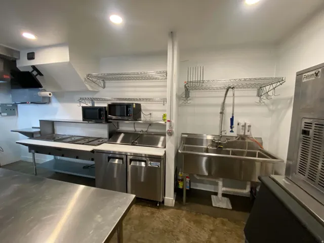 Stainless steel work surfaces, commercial-grade sink, under-counter refrigeration, and overhead shelving for storage