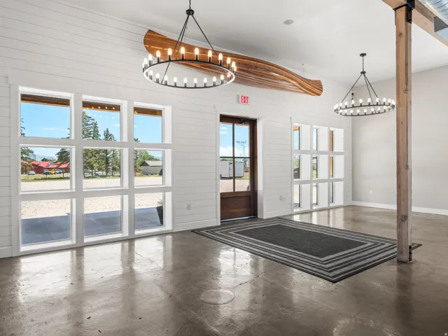 Polished concrete flooring, shiplap accent walls, two large multi-pane windows, a substantial wood support beam, and two circular chandeliers