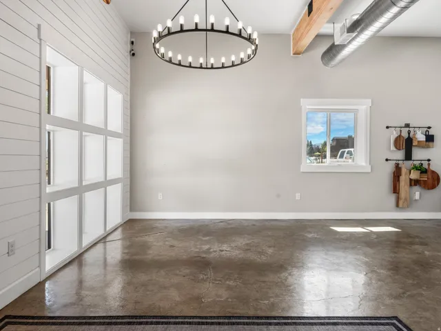 Exposed concrete flooring, overhead wood beam, exposed ductwork, and a circular chandelier with multiple bulbs