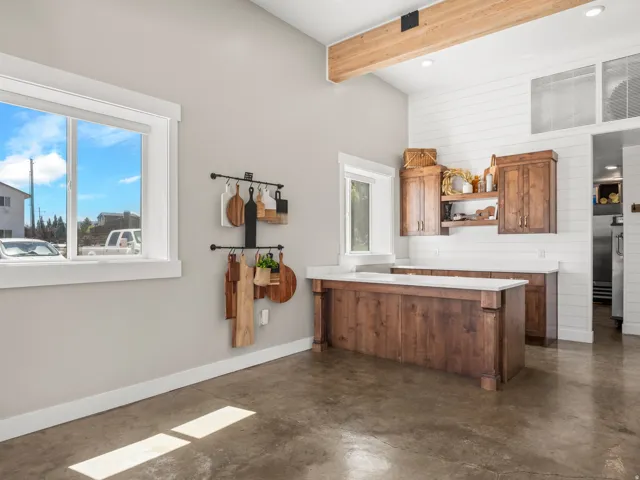 Vaulted ceilings with exposed wood beams, wood-finish cabinetry, white countertops, shiplap accent wall, and polished concrete flooring