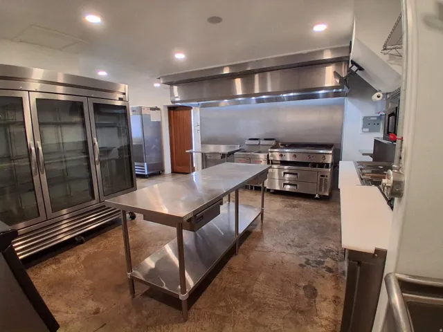 Stainless steel kitchen island, expansive stainless steel refrigerator units, commercial-grade range with griddle, stainless steel exhaust hood, and concrete flooring