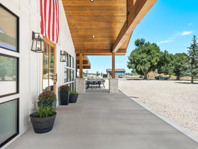 Expansive covered porch featuring a wood-finish ceiling, stone-clad columns, and concrete flooring
