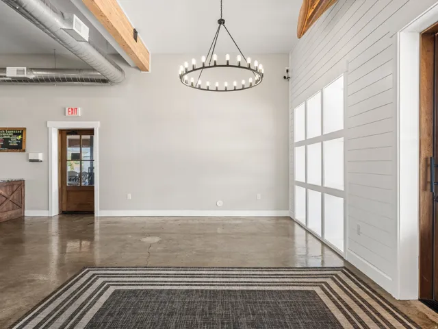 Polished concrete flooring, exposed ceiling ductwork, high ceilings with wood beams, a modern circular chandelier, and a shiplap accent wall with integrated windows