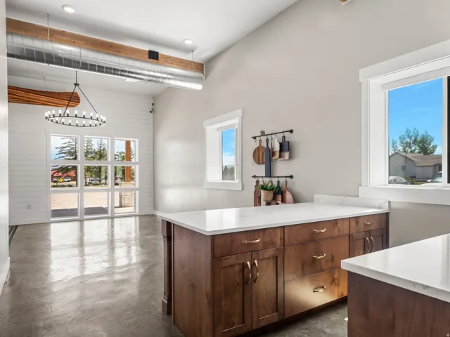 Polished concrete flooring, vaulted ceilings with exposed ductwork, wood-finish cabinetry with light countertops, and expansive windows