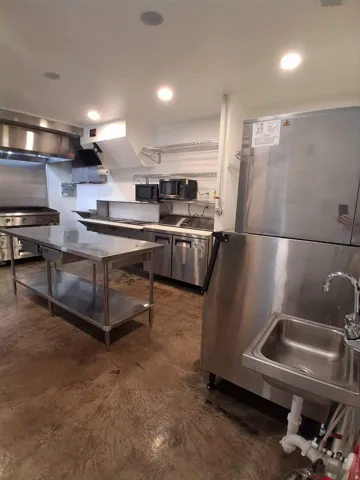 Stainless steel commercial kitchen with a large griddle, built-in shelving, and concrete flooring