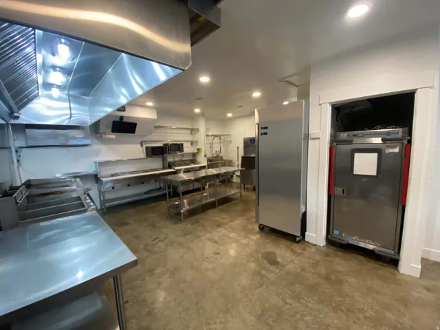Commercial kitchen featuring extensive stainless steel countertops, industrial ventilation hood, recessed lighting, and durable concrete flooring
