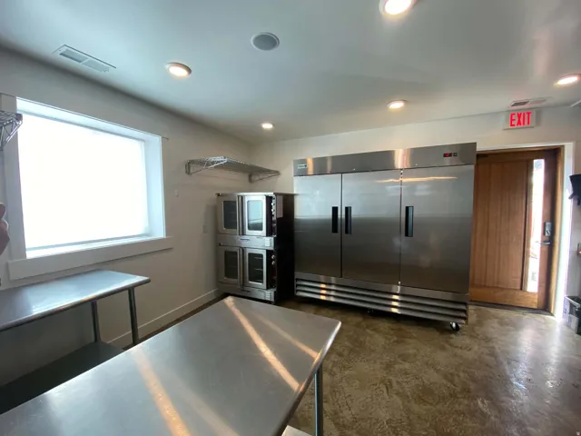 Stainless steel commercial refrigeration unit, stainless steel work surfaces, window with natural light, recessed lighting, and a wood-paneled door