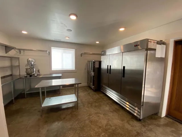 Commercial-grade stainless steel appliances and work surfaces, concrete flooring, recessed lighting, and a single window