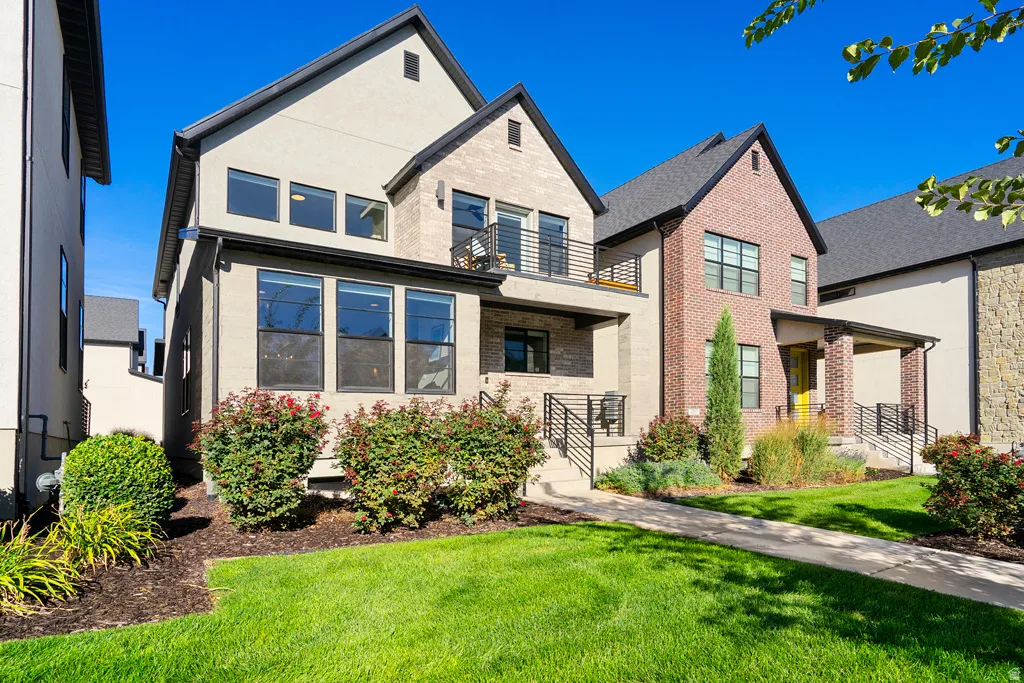 Contemporary exterior with a gabled roofline, brick and stucco siding, multiple large windows, and a second-story balcony with metal railings