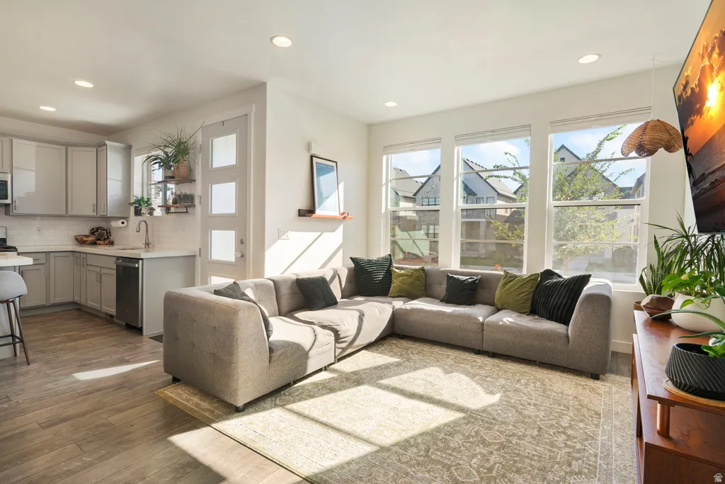 Recessed lighting, wood-finish flooring, light grey cabinetry, stainless steel dishwasher, and multiple windows with roller blinds