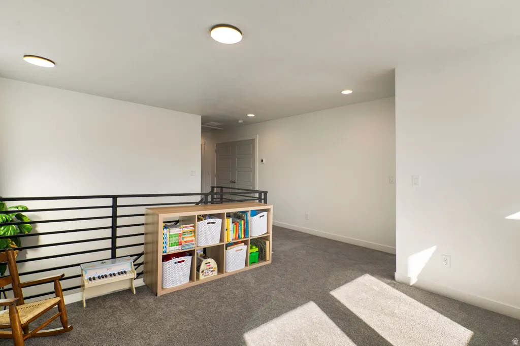 Carpeted open loft space with contemporary black metal railing and recessed lighting