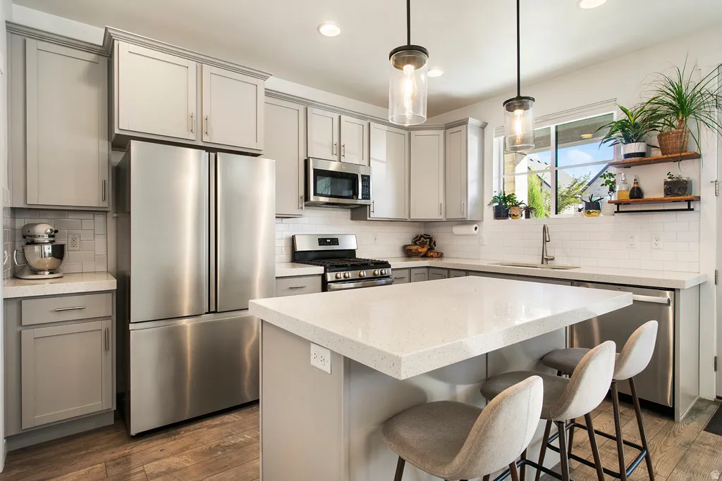 Kitchen featuring a center island with countertop seating, stainless steel appliances, light gray cabinetry, and subway tile backsplash