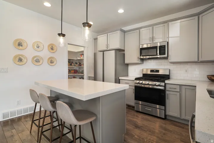 Kitchen featuring a central island with countertop seating, stainless steel appliances, light gray cabinetry, subway tile backsplash, and wood-finish flooring