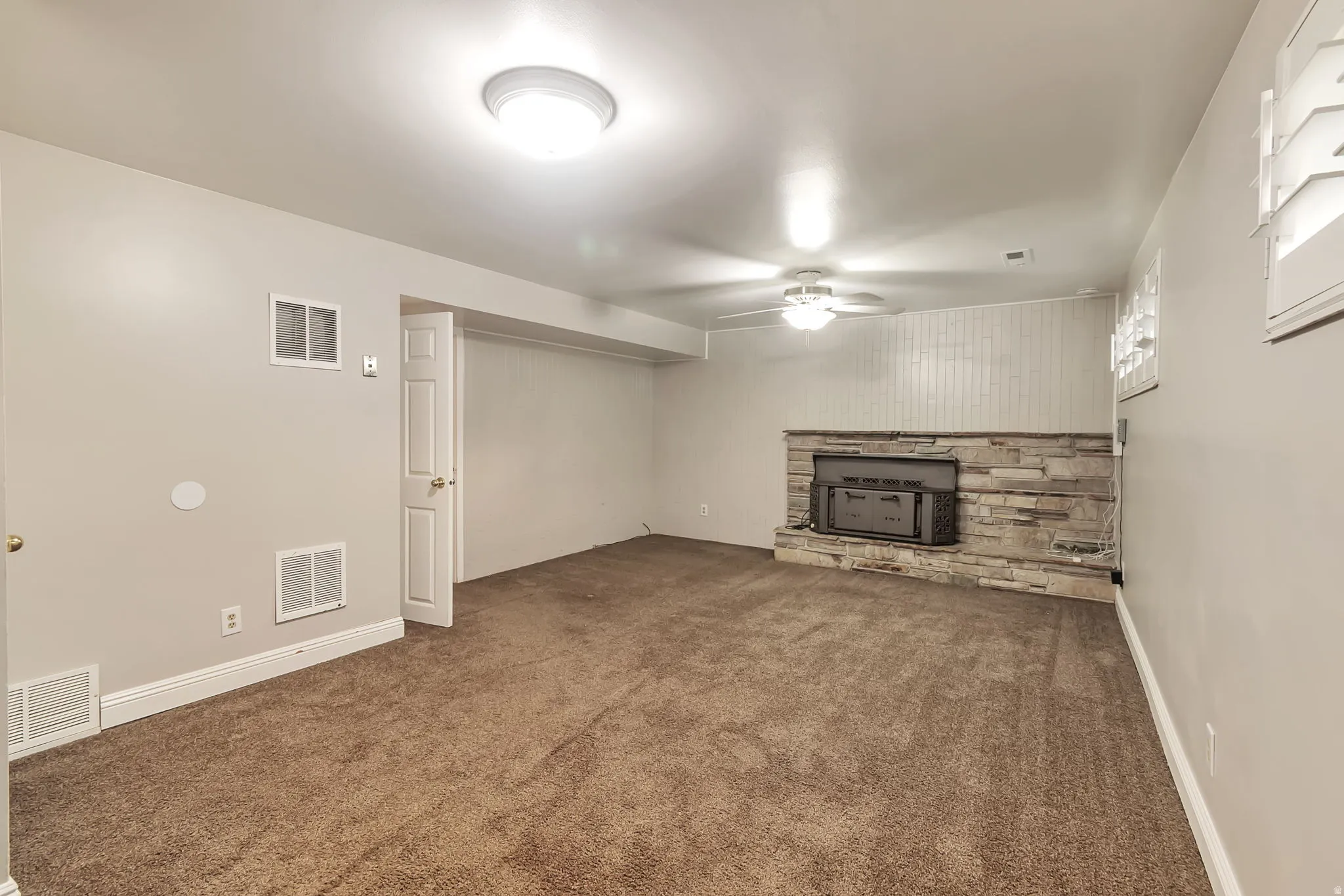 Carpeted family room featuring a stone-fireplace and hearth