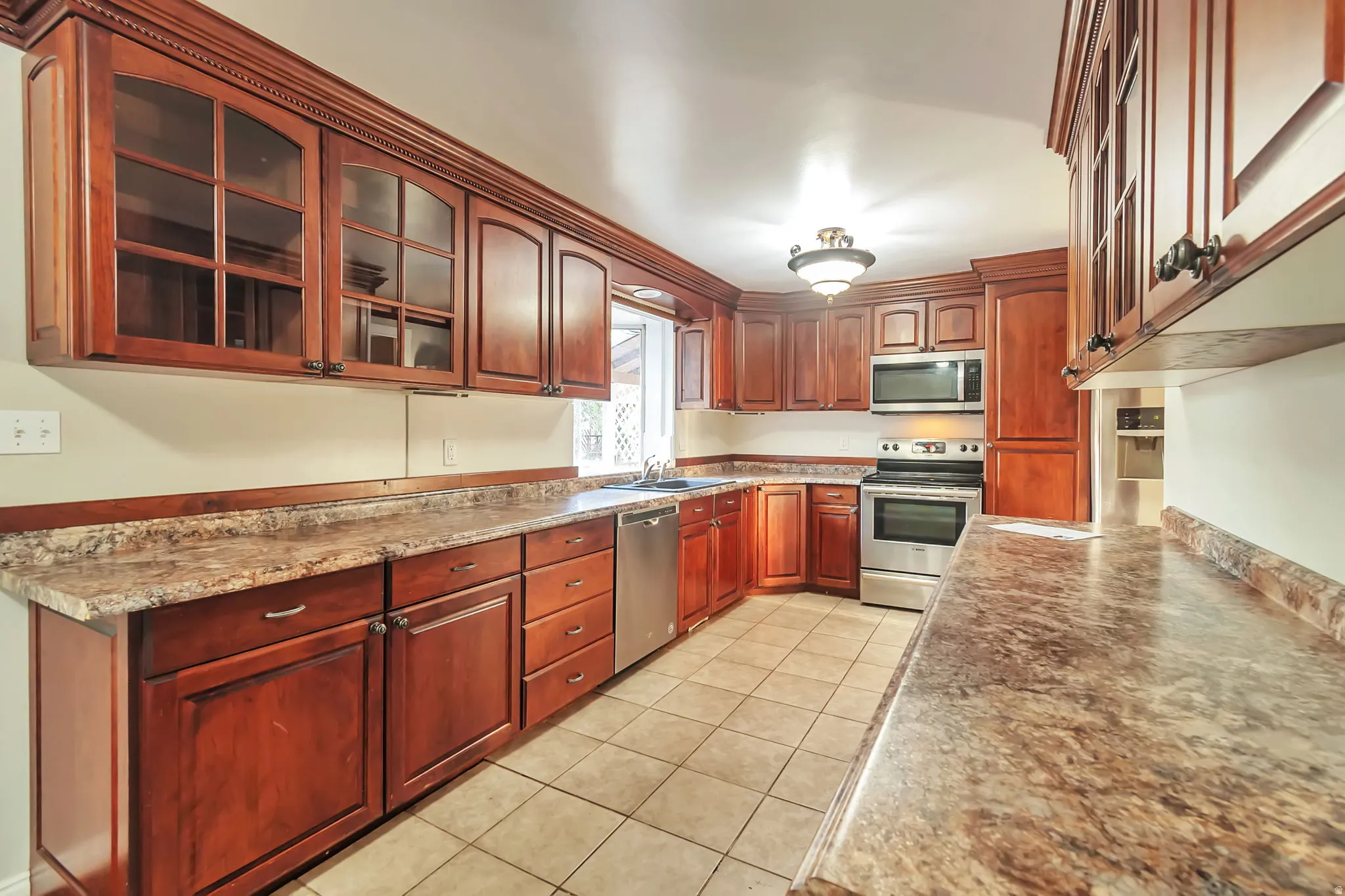 Wood-finish cabinetry, patterned countertops, stainless steel appliances, tile flooring, and an integrated stainless steel sink