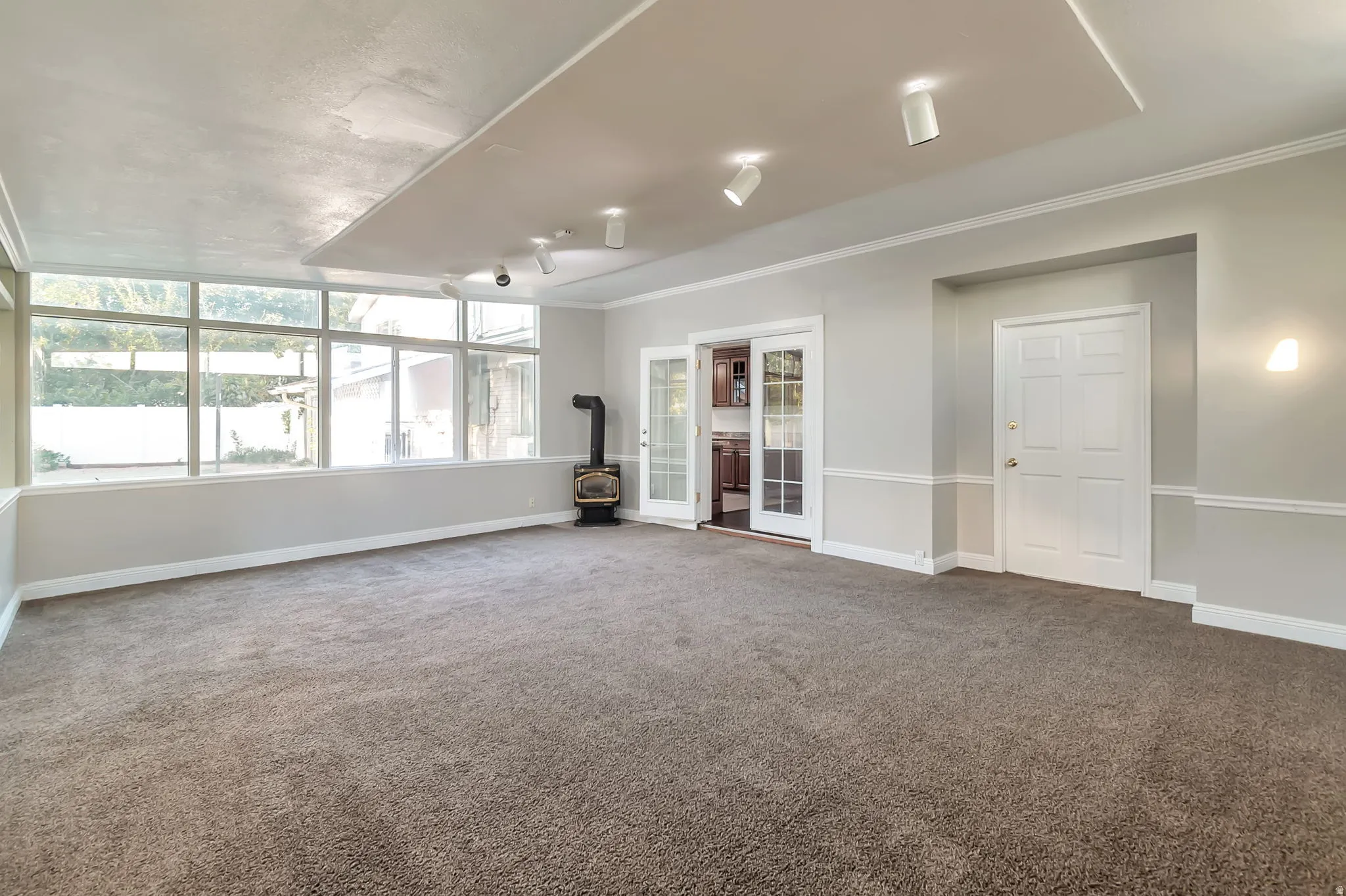 Bright family/sun room with a wood-burning stove, large pane windows, recessed ceiling lighting, and French doors
