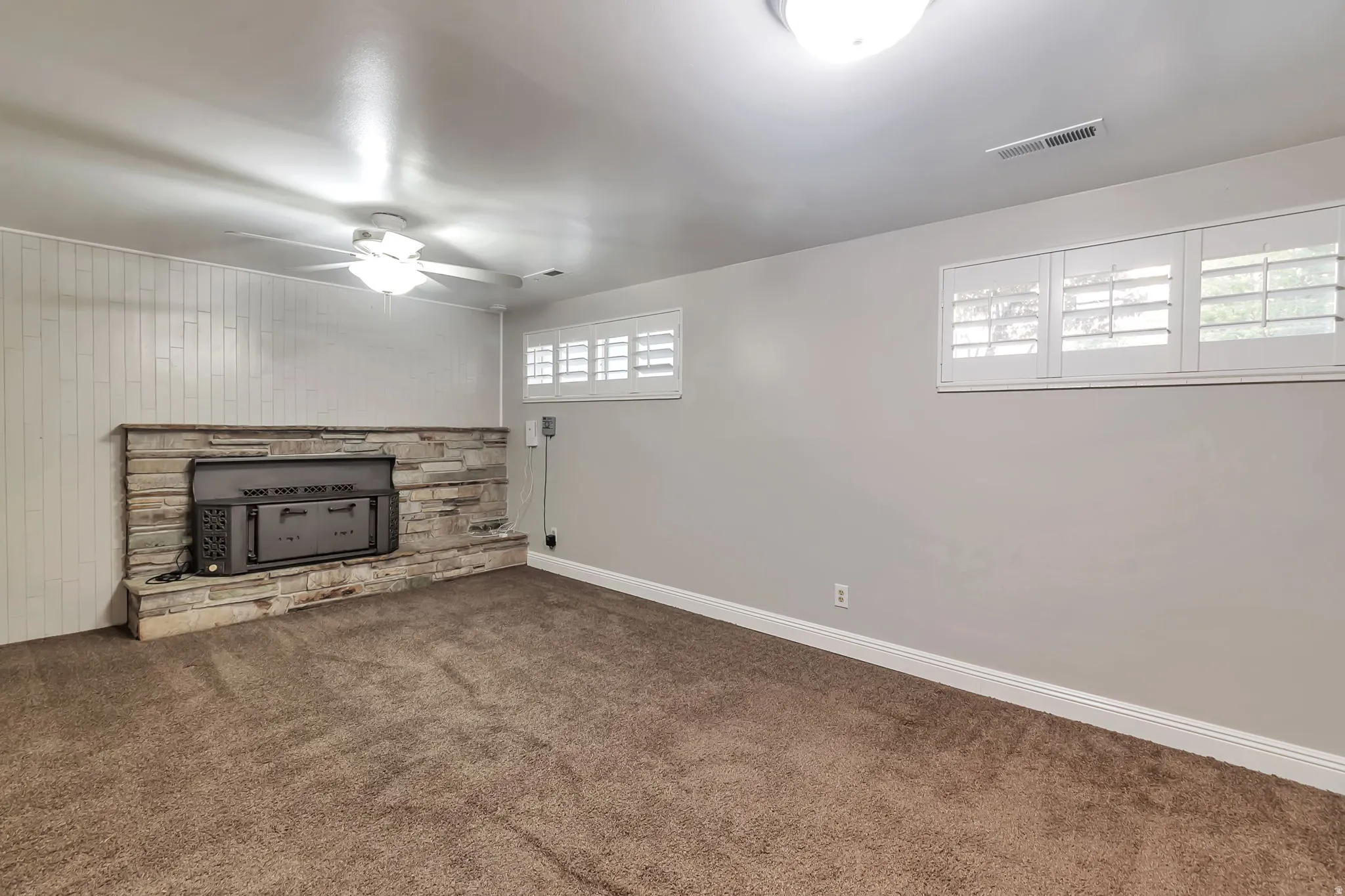 Stone surround fireplace, white plantation shutters, neutral wall color, ceiling fan, and recessed lighting