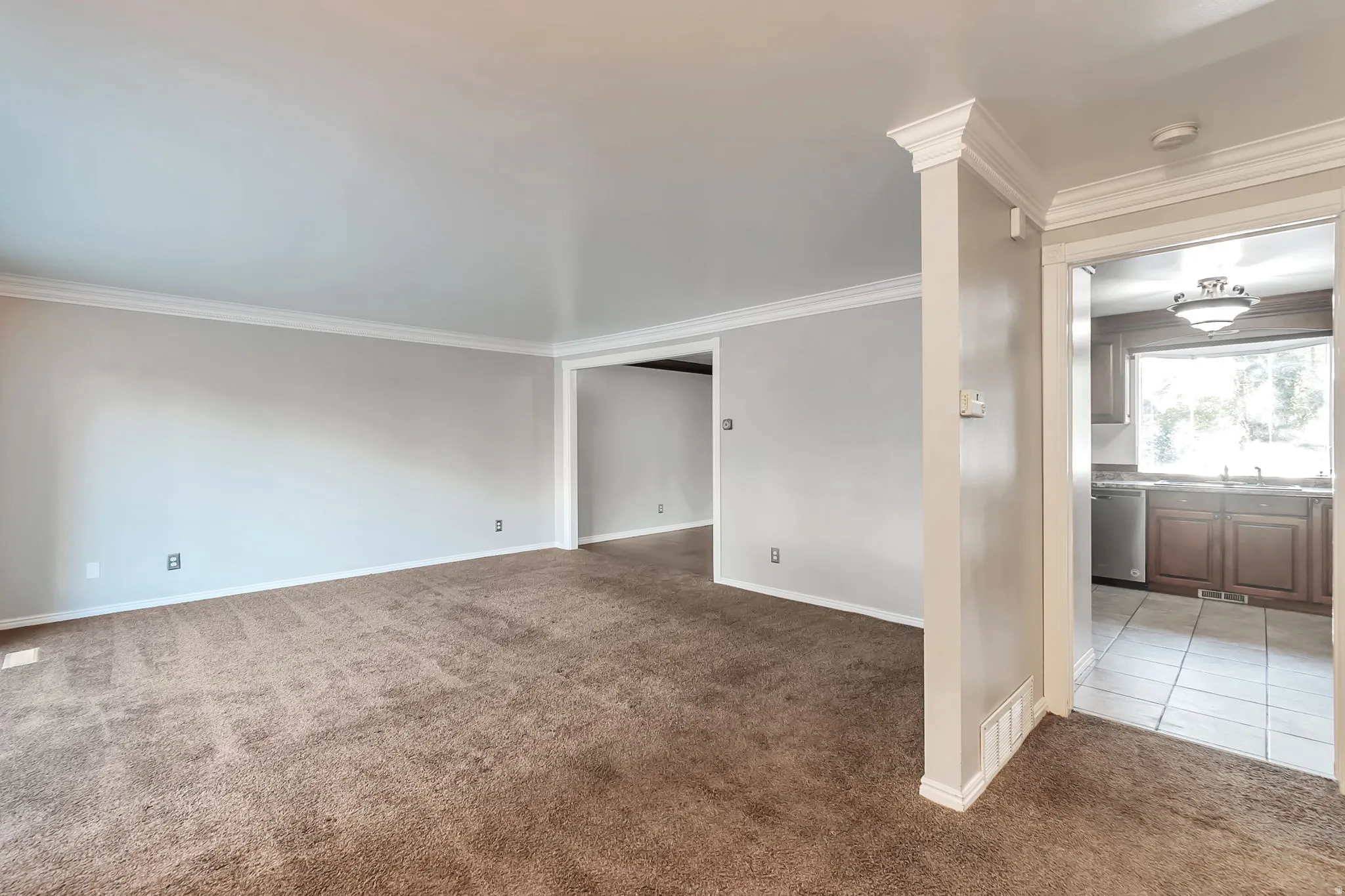Open concept living area with carpeting, crown molding, and a partial archway