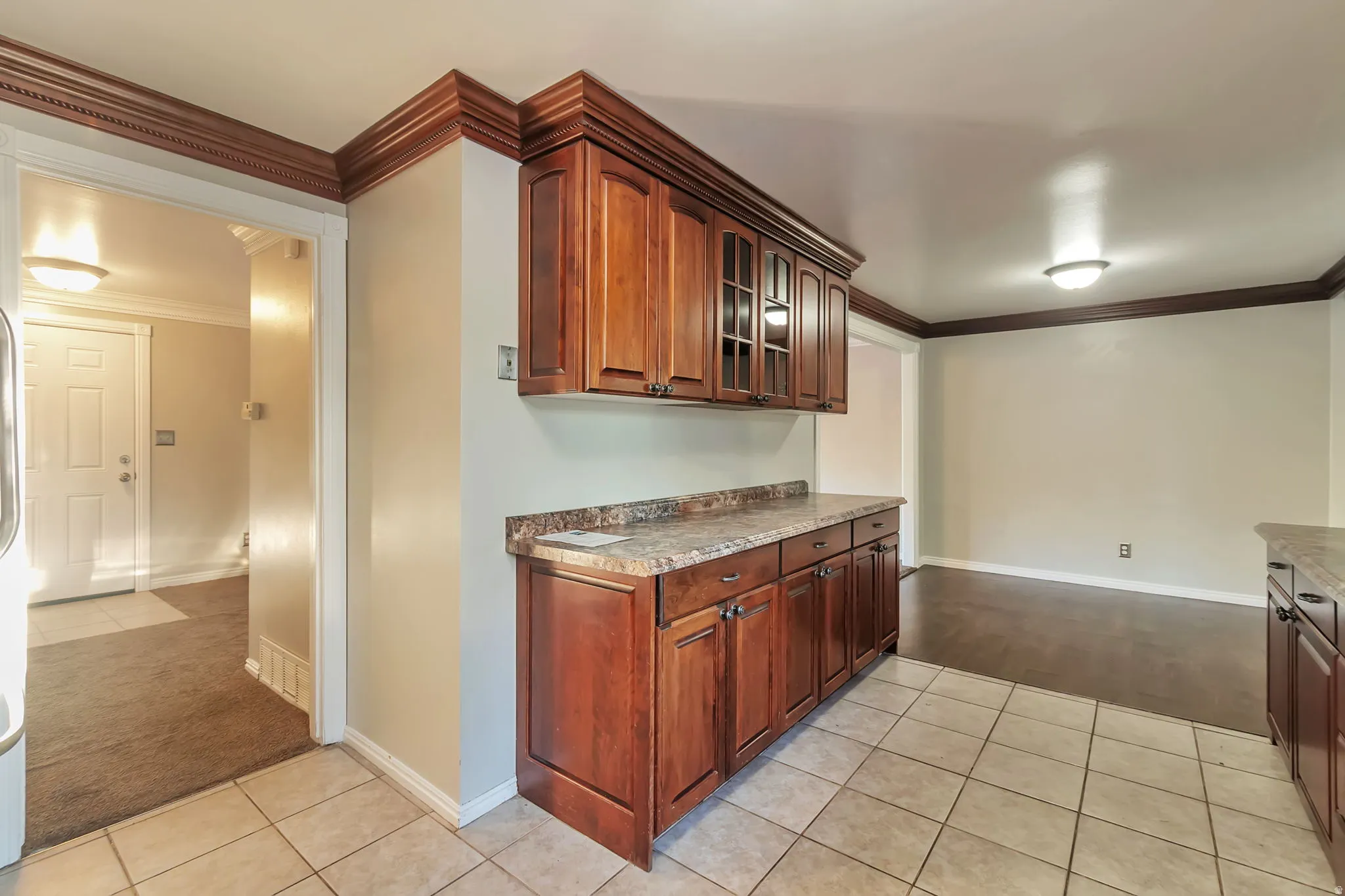 Wood-finish cabinetry with glass-front uppers, laminate countertops, tiled flooring, and crown molding