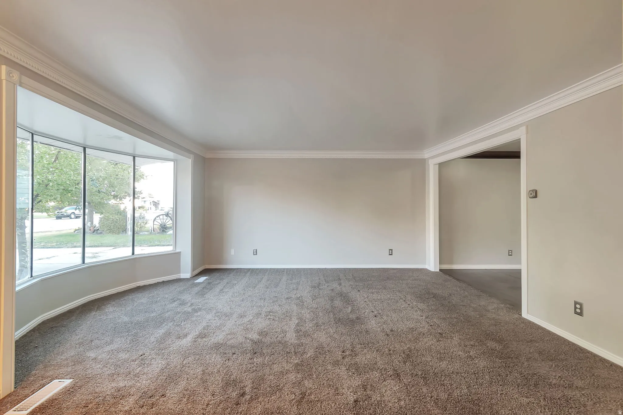 Curved bay window, crown molding, wall-to-wall carpeting, wide archway, and neutral wall tones