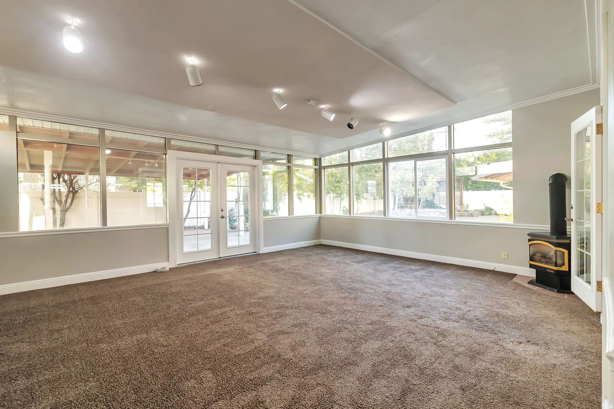 Expansive family/sun room featuring wall-to-wall carpeting, multiple windows, French doors, track lighting, and a built-in stove
