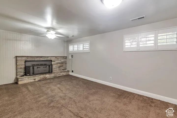 Stone surround fireplace, white plantation shutters, neutral wall color, ceiling fan, and recessed lighting