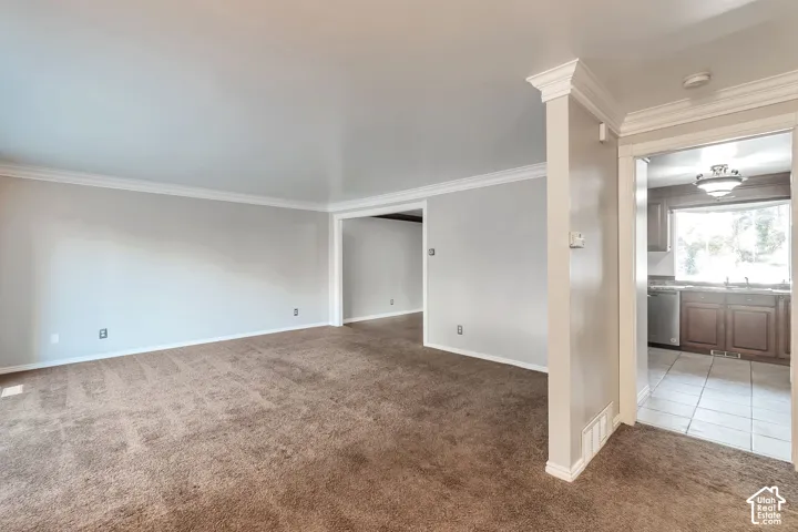 Open concept living area with carpeting, crown molding, and a partial archway