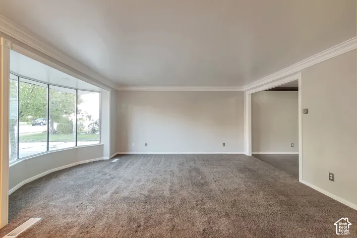 Curved bay window, crown molding, wall-to-wall carpeting, wide archway, and neutral wall tones