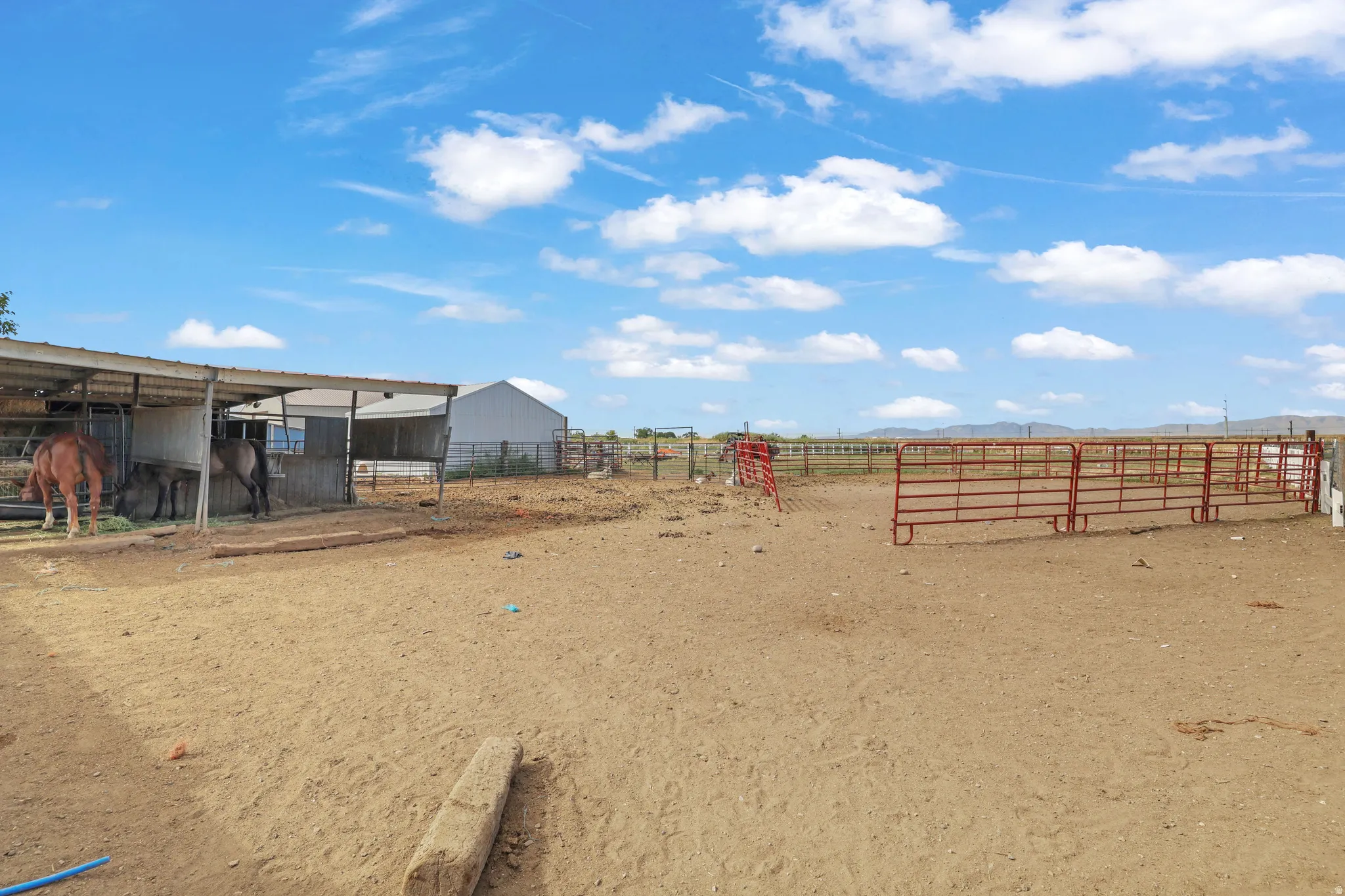 Expansive outdoor area featuring a covered structure, a white outbuilding, and multiple red metal fencing sections