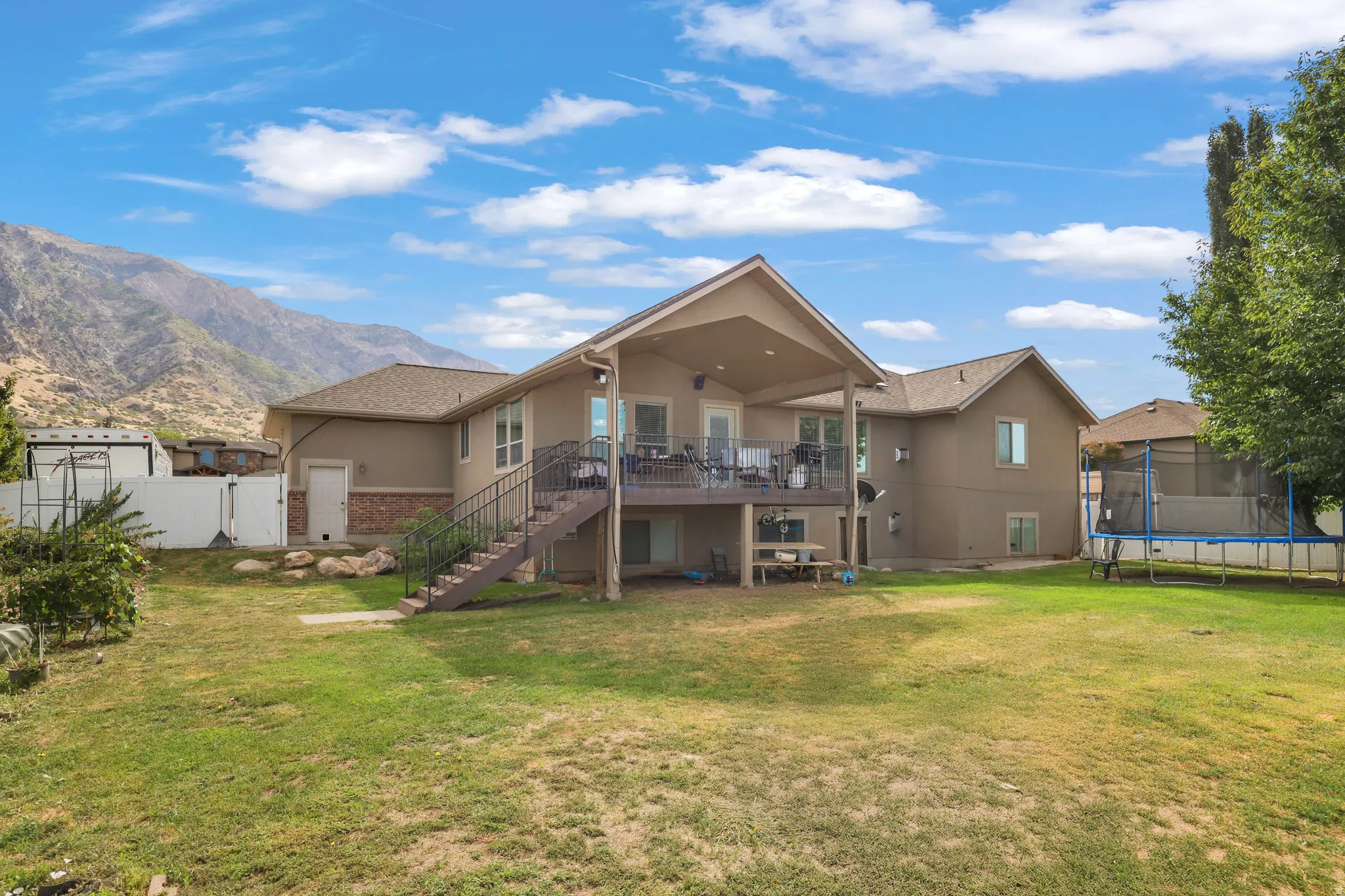 Expansive backyard featuring a covered upper deck, lower patio area, and stucco exterior with brick accents