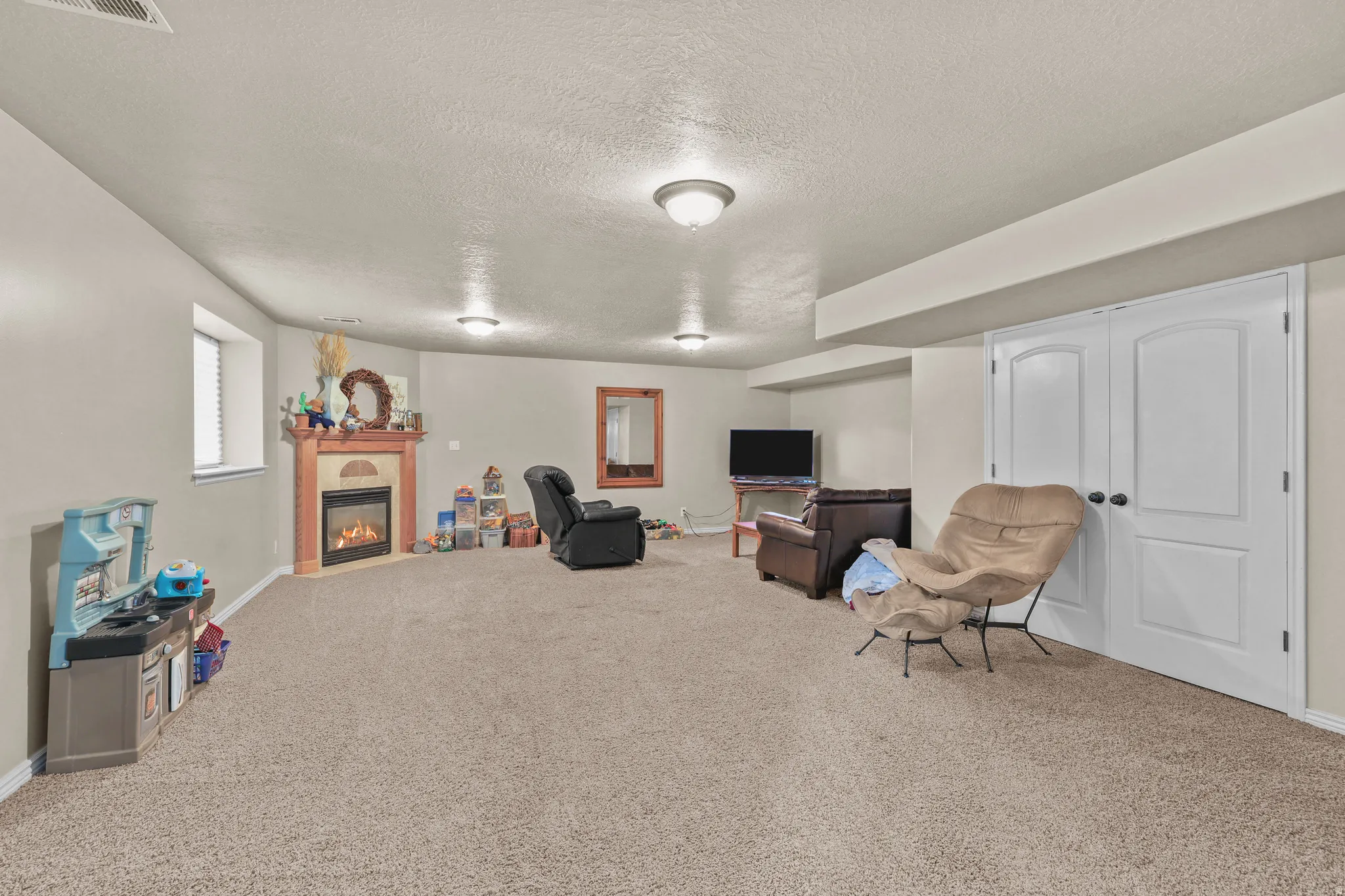 Recessed corner fireplace with a mantel, carpeted flooring, and an egress window