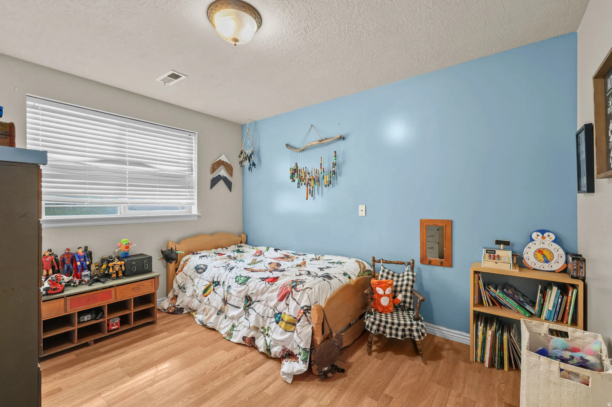 Wood-finish flooring, single window with blinds, ceiling-mounted light fixture, light blue wall accent