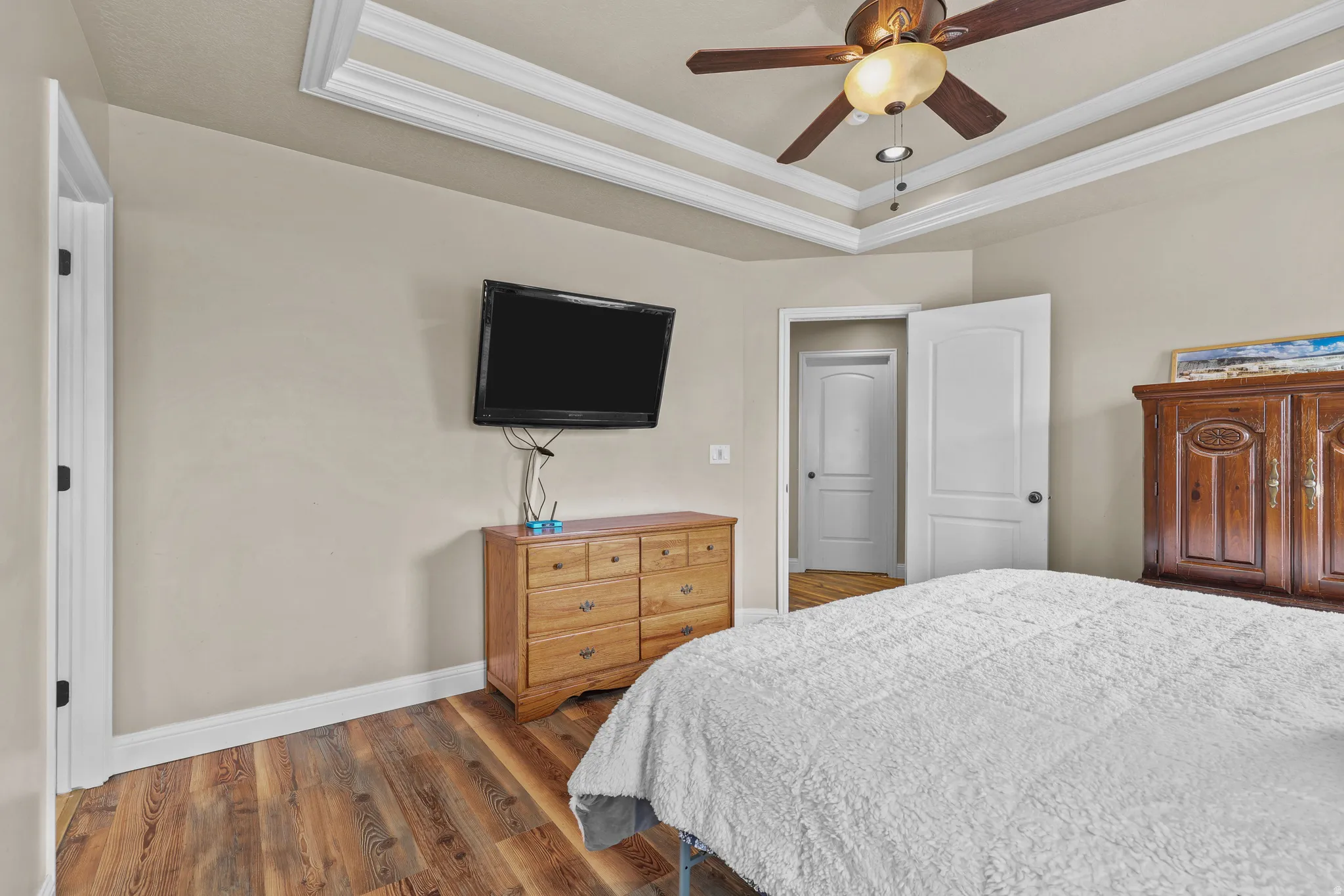 Tray ceiling with crown molding, wood-finish flooring, ceiling fan with integrated lighting, and white interior doors