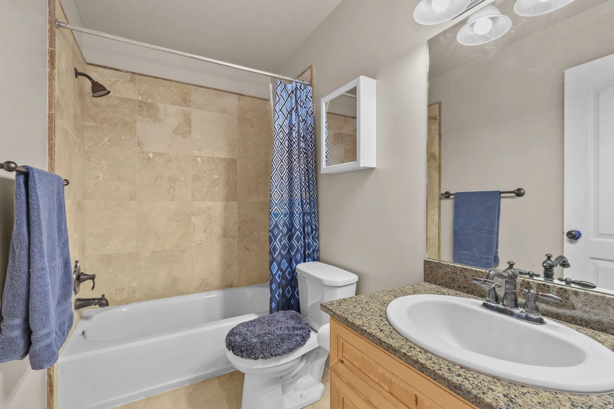 Bathroom featuring a wood-finish vanity with a granite countertop, undermount sink, and a framed mirror
