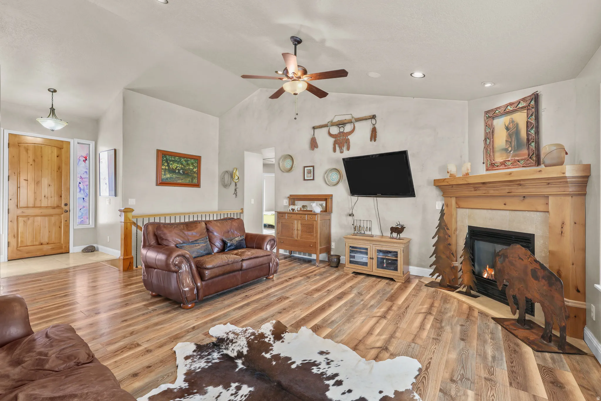 Vaulted ceiling with a ceiling fan, wood-finish flooring, built-in fireplace with a wood mantel, recessed lighting, and a wood entry door