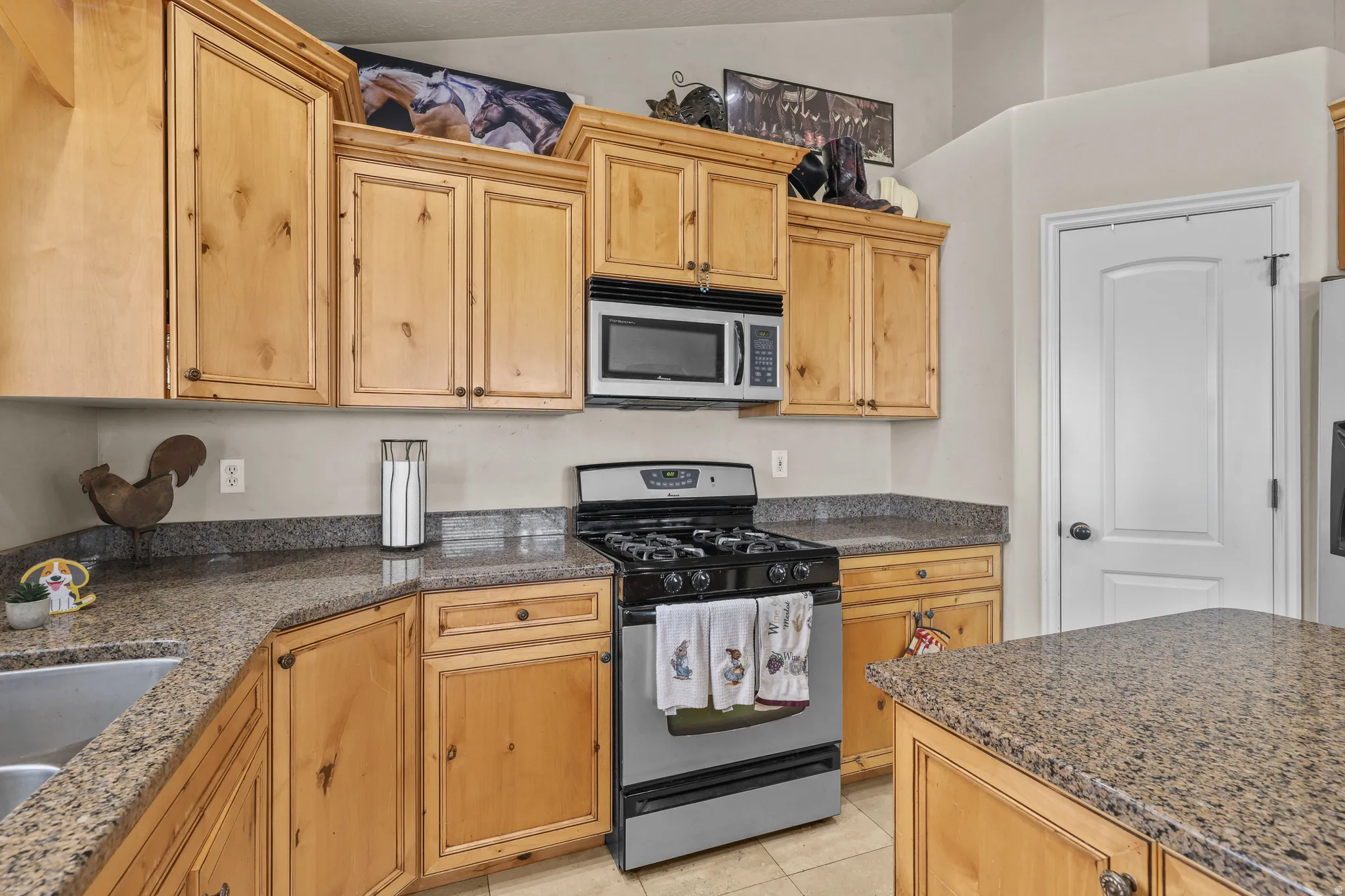 Kitchen featuring light wood-finish cabinetry, speckled countertops, a stainless steel gas range, and an integrated microwave