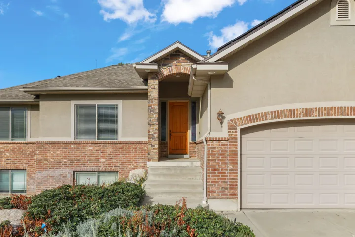 Exterior featuring brick and stucco finishes, an arched entry, a paneled garage door, and a covered front entry with stairs