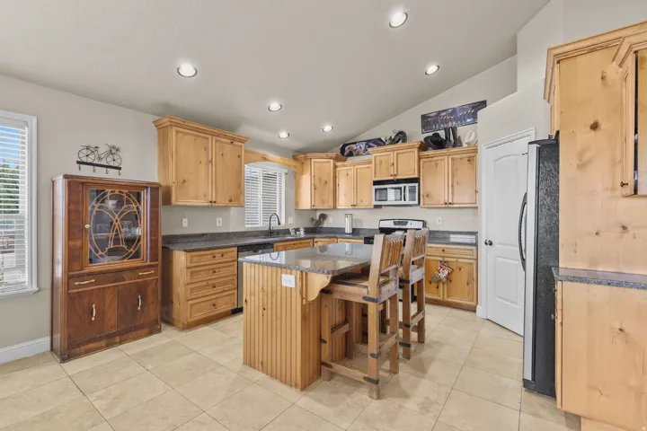 Kitchen featuring natural wood cabinetry, stone countertops, recessed lighting, a kitchen island with seating, and tile flooring